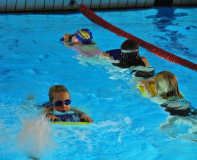 4 junge Schwimmer mit Brettern auf einer Bahn